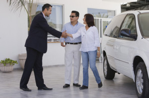 Hispanic couple shaking hands with car salesman